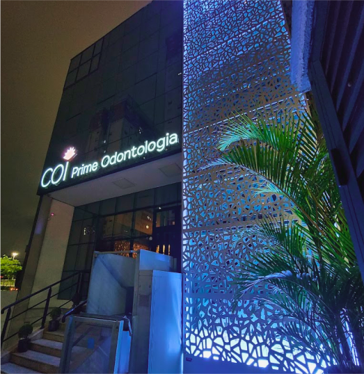 A faixada da clínica a noite com uma luz azul e o letreiro onde está escrito COI Prime Odontologia aceso com uma luz branca